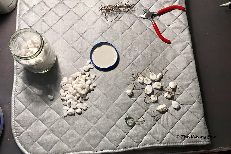 a jar of small white rocks with a pile of small white rocks, a pair of cutting pliers, and a pile of wire to make hooks