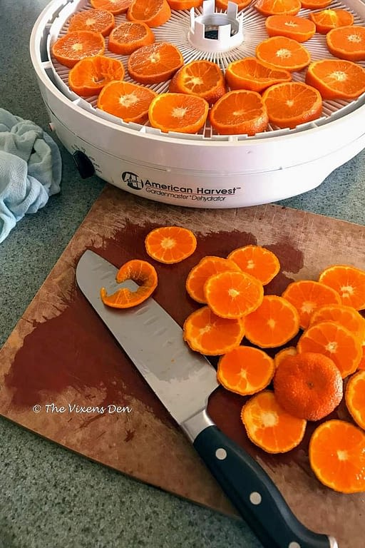 sliced oranges on a cutting board with a knife and a dehydrator with a tray of orange slices