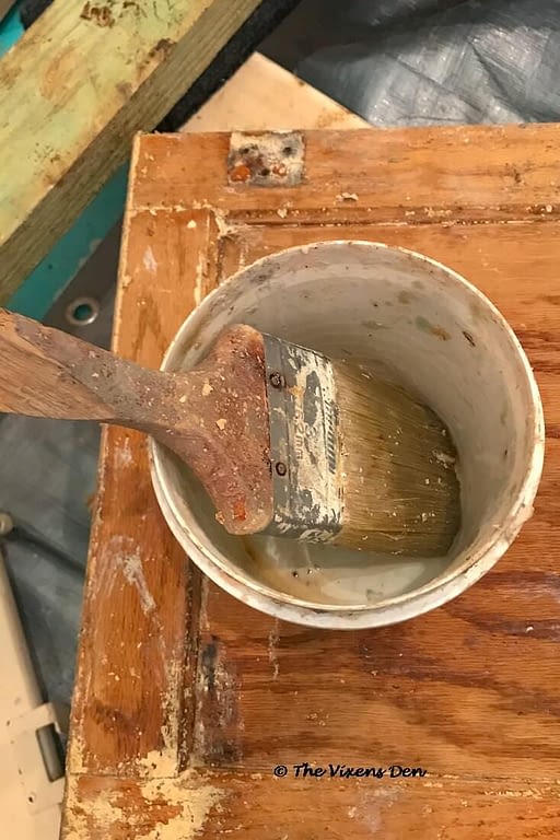 a plastic container with finish remover in the bottom and a paint brush