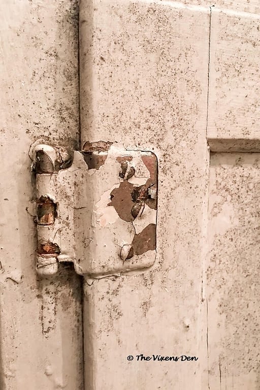 old cabinet door hinge covered with flaking paint