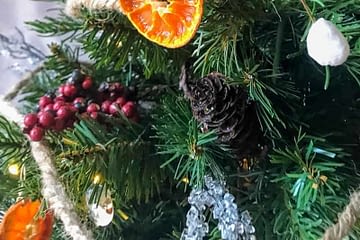 closeup showing DIY dried orange slices on a mini Christmas tree decorated with pinecones, berries, DIY rustic ornaments, and ice twigs